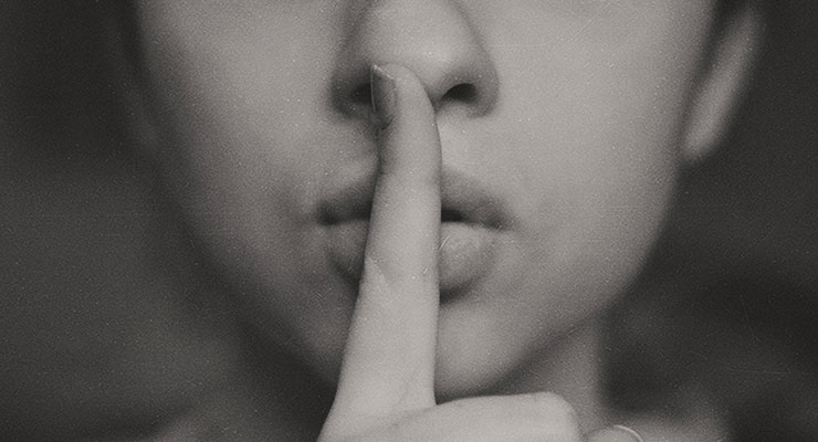 Silent Communication: Honoring the Space Between the Words by Doris Schachenhofer. Photograph of a women with a finger in front of her mouth signaling quiet, by Kristina Flour