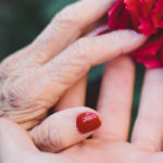 The simultaneous passing of her grandmothers offered a pregnant woman a deeper understanding of life, love, and the divine path of our maternal DNA by Liz Tenety. Photograph of older hand holding younger hand with rose by Jake Thacker