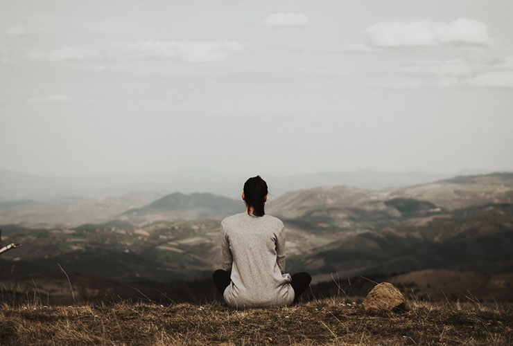 Tending Our Emotional Stew Through Mindful Acceptance by Scott Cooper. Photograph of person meditating on mountain top by Milan Popovic