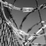 Writing From The Inside Out: Incarceration Through The Lens Of Humanity by Gretchen Primack. Photograph of a barbed wire prison fence by Robert Hickerson.