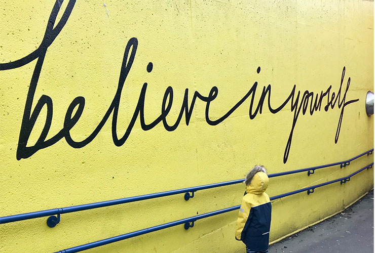 Why You Need a Life Coach by Blaze Schwaller. Photograph of a child looking at wall mural that reads "believe in yourself" by Katrina Kaif