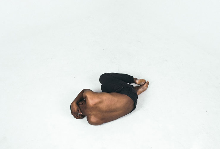 Managing Stress Through Communication and Lifestyle Changes by Anna Kucirkova. Photograph of a man in a fetal position on the floor by Mwangi Gatheca