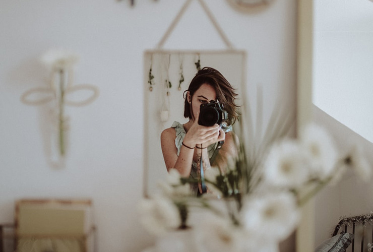 Why 'Trying Harder' To Prioritize Yourself Just Doesn't Work by Leila Ansart. Photograph of a woman photographing herself in the mirror by Kinga Chichewicz.