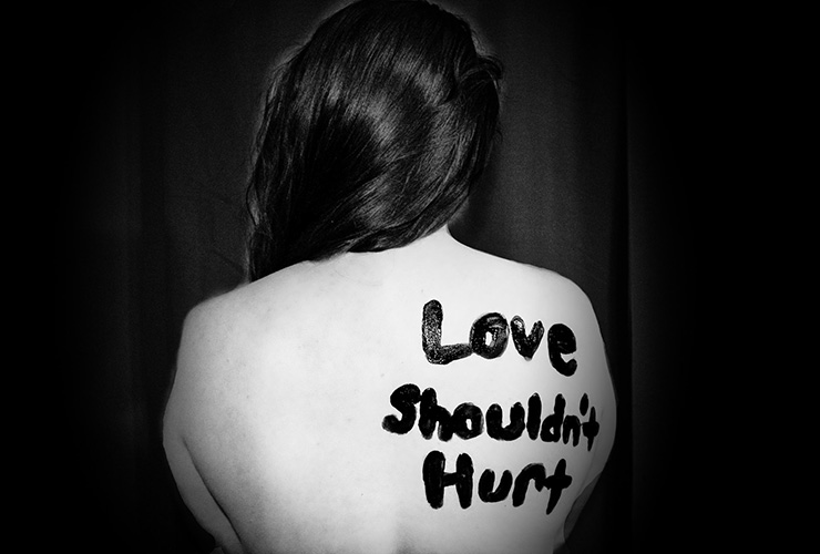 Truth Be Told: Healing from a Traumatic Relationship Can Only Come from Honesty by Tassal Shanebrook. Photograph of a woman's back with "Love Shouldn't Hurt" painted on it by Sydney Sims