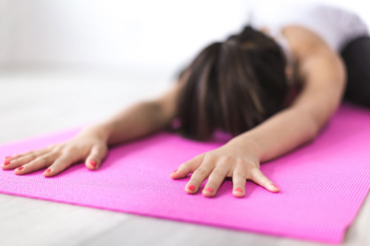 Photograph of a woman in Childs pose on a pink mat