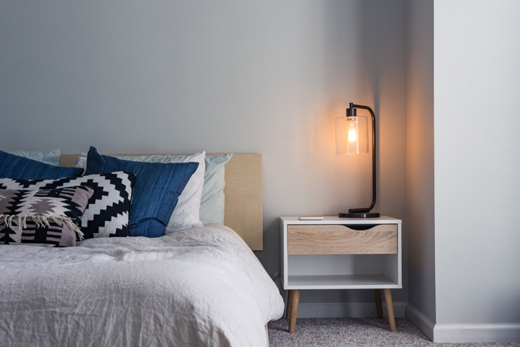 Photograph of a bed, nightstand and lamp by Christopher Jolly