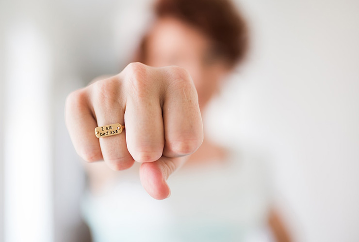 Healing Your Cervix: Tapping into Your Innate Power of Self-Healing by Denell Nawrocki. Photograph of a woman fist with a ring that reads "I am badass" by Brooke Lark