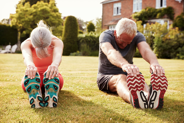 Health-Boosting, Low-Impact Exercises for Seniors, by Jenny Hart. Photograph of two seniors stretching on lawn by Monkey Business