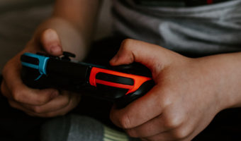 Kids, Quarantine & Devices: Managing Screen Time During COVID and Beyond by Joshua Wayne. photograph of a child holding a video game controller by Kelly Sikkema.