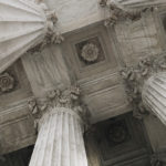 Politics: Palliative Care For A Curable Disease? By Olga Sheean. Photograph of the pillars and ceiling of a government building by Anna Sullivan.