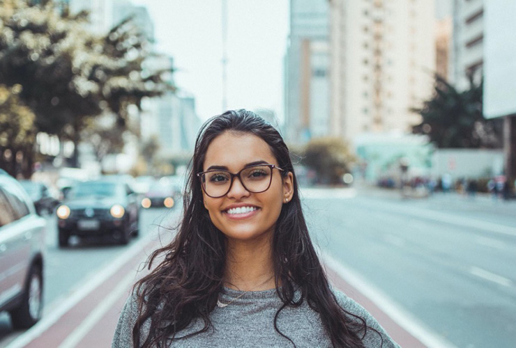 Why You Need To Be More Selfish In 2021 by Laura May. Photograph of a woman in glasses smiling in NYC; Photograph by Daniel Xavier, courtesy of Pexels