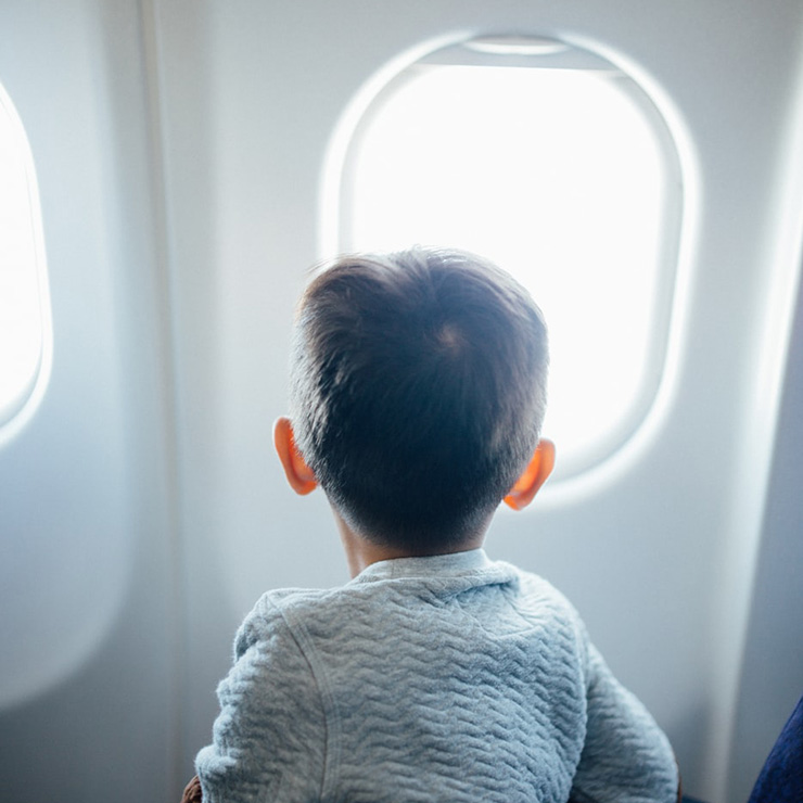 A Guide for Traveling with Kids Because Life Shouldn’t Stop! by Rachel Hudson. Photograph of a child looking out a plane window by Hanson Lu