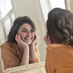 The Most Beautiful Thing You Can Wear is Confidence by Holly Schaefer. Photograph of a girl smiling at herself in the mirror by Andrew Piacquadio