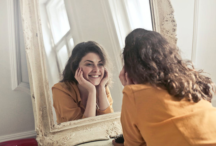 The Most Beautiful Thing You Can Wear is Confidence, by Holly Schaefer. Photograph of a girl smiling at herself in the mirror by Andrew Piacquadio