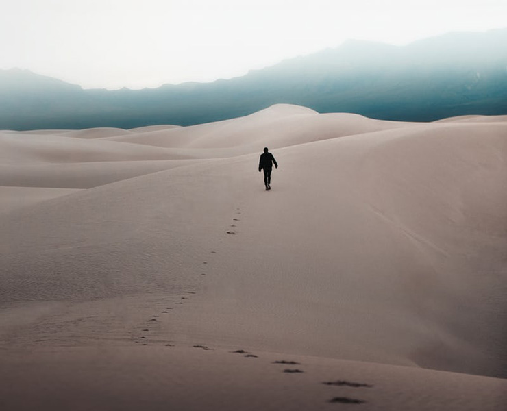 The Art of Walking in Someone's Shoes by Judy Marano. Photograph of a person leaving footprints, walking across sand dunes by Logan Armstrong