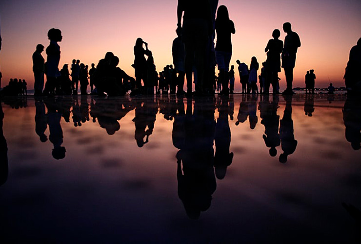 It Takes a Village: A Look at the Parental Community from Africa to Your Home, by Judy Marano. Photograph of people standing on the beach after sunset by Mario Purisic