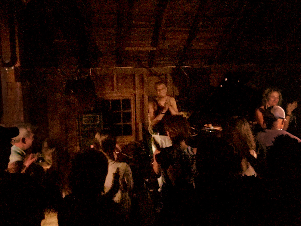 In the Dark: An Unexpectedly Spiritual Evening of Jazz with Jack DeJohnette, by Bill Miles. Photograph of dimly lit barn with Jack DeJohnette thanking the audience after a performance.