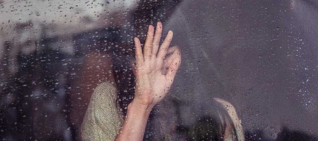 Grief as a Catalyst for Personal Reinvention, by Sweta Vikram. Photograph of woman with hand against window in rain by Milada Vigerova.