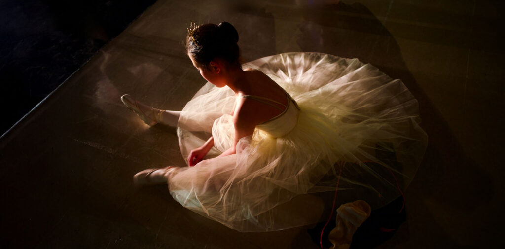 Young ballerina sitting on stage, contemplating her challenges